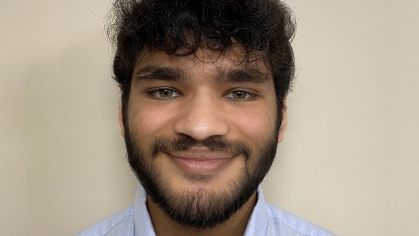 Head shot of male student with curly black hair and a beard wearing a light blue collared shirt.