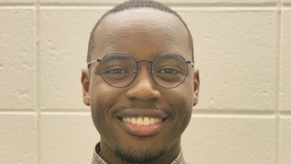 Head shot of Black young man wearing glasses and a light brown collared shirt.